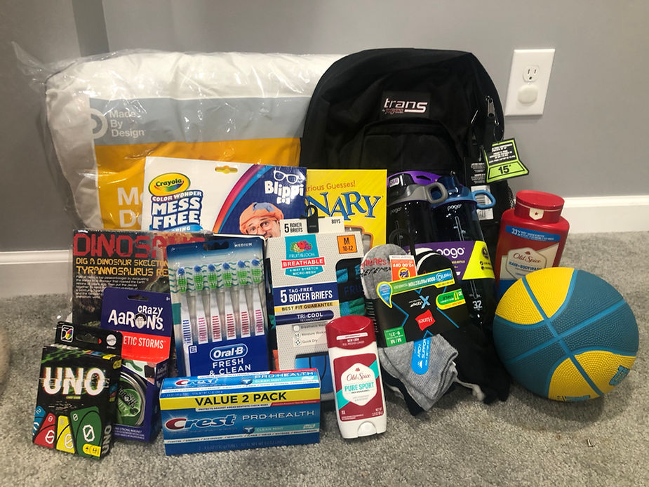 An assortment of items including a basketball, backpack, hygiene products, and children's toys laid out neatly on a gray carpeted floor.