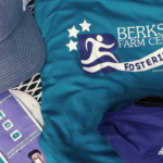 Assorted promotional items including a cap, t-shirts, and pamphlets from berkshire farm center, themed in blue and purple colors with logos and text.