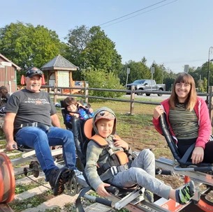A family enjoys a ride on pedal-powered rail bikes. a man, woman, and two children, one wearing a helmet, are seated on tandem bikes on train tracks, surrounded by greenery.