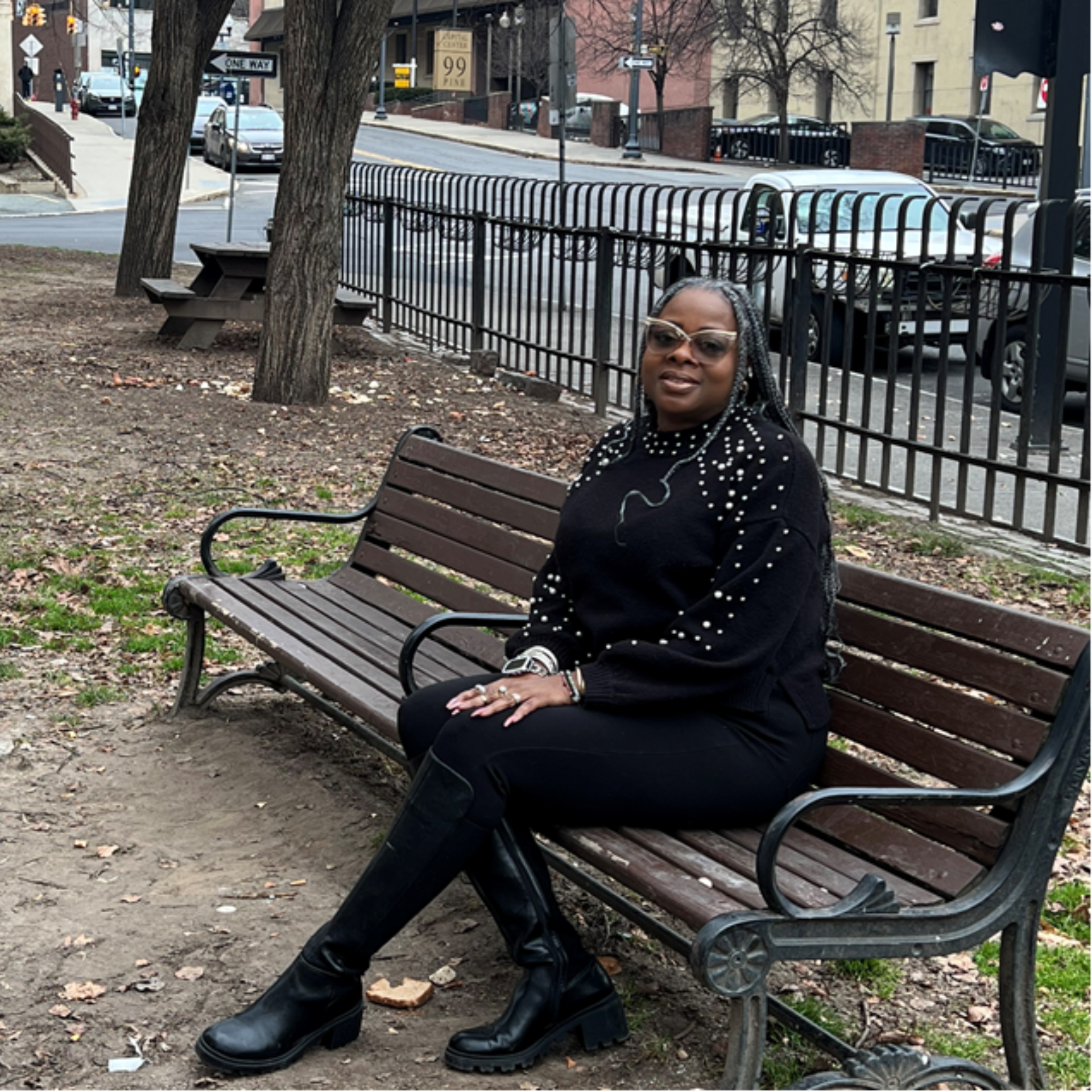 Sahoutah on a park bench dressed in black clothes, smiling.